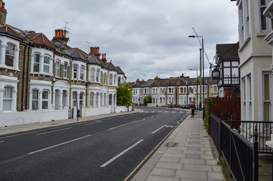 A row of Victorian terraced houses in New Barnet, featuring decorative bay windows, ornate metalwork on small balconies, and brick facades with gabled roofs under a clear blue sky. The properties are 